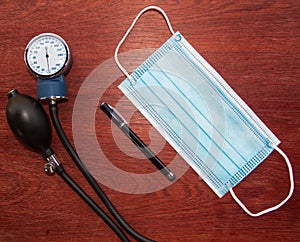 medical blue mask with pen and manual blood pressure reader with wood background representing work of doctors