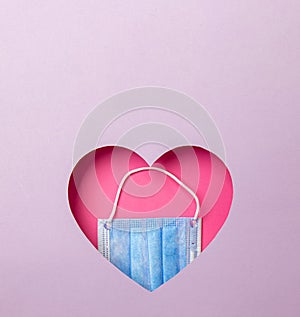 The medical blue mask is in a pink heart on a purple background. Minimal concept of love and medicine. Copy space