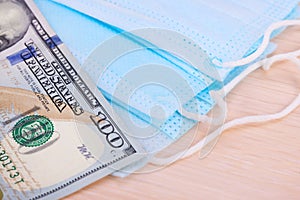 Medical blue masks and one banknote of 100 dollars,lying on light background.Soft focus.Concept of protection, deficiency, high