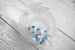 Medical blue pills and white bottle on white wooden background.