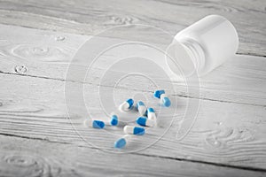 Medical blue pills and white bottle on wooden background.