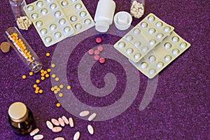 Medical bottles and medication pills spilling out on to purple background