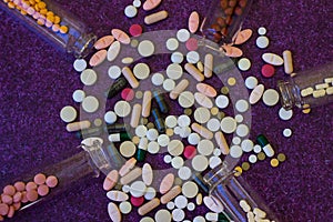 Medical bottles and medication pills spilling out on to purple background