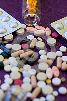 Medical bottles and medication pills spilling out on to purple background