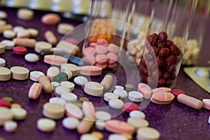 Medical bottles and medication pills spilling out on to purple background