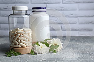 Medical bottles with pills and white flowers on light gray textured table, space for text