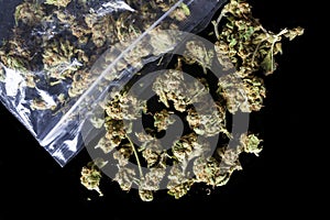 Medical cannabis buds scattered from package on black from above