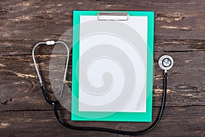 Medical clipboard and stethoscope on dark wooden table.