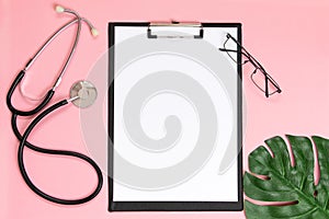 Medical clipboard, stethoscope, monstera sheet and face shield on a pink background. Medical banner template with copy space,