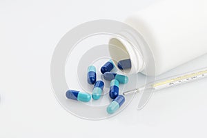 Medical : Close up of Blue Capsules with Bottle and Analog Thermometer on White Background Shot in Studio.