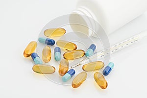 Medical : Close up of Yellow and Blue Capsules with Bottle and Analog Thermometer on White Background Shot in Studio.