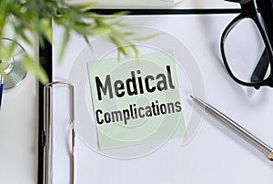 Medical complications text on notepad with stethoscope, glasses and pen.