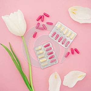 Medical composition with vitamins pills and white flowers on pink background. Flat lay