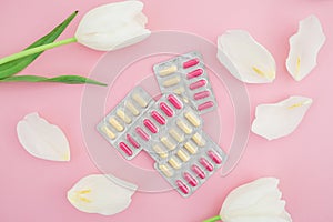 Medical composition with vitamins tablets and white flowers on pink background. Flat lay, top view.