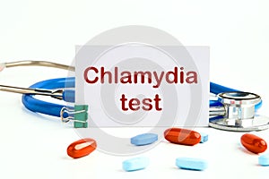 Medical concept. Chlamydia Test text on a white business card on a white background next to a stethoscope and pills, vitamins