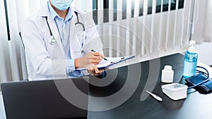 Medical concept a male doctor wearing a mask writing prescription to patient at his modern clinic for recovering from Coronavirus