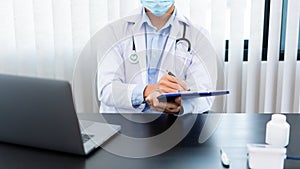 Medical concept a male doctor wearing a mask writing prescription to patient for recovering from Coronavirus COVID-19 at his