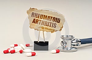 Near the stethoscope are pills and a clip with a cardboard sign - Rheumatoid arthritis photo