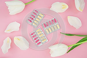 Medical concept with vitamins pills and white flowers on pink background. Flat lay, top view.