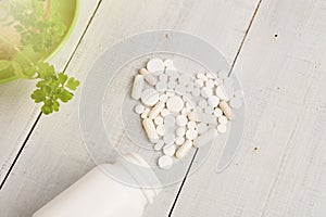 Medical concept - white heart of pills and capsules on white woo