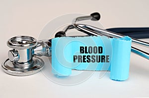 On a white surface lies a stethoscope and a blue roll of paper with the inscription - Blood Pressure