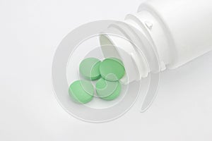 Medical conceptual photo. Green round pharmaceutical pills spilling out of a white pill bottle.