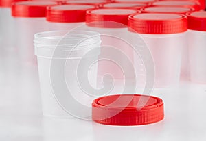 Medical container for the collection of tests with an open lid next to it in the background of other containers. Concept