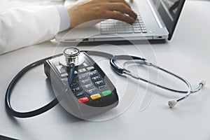 medical costs and health care expenses concept - payment terminal with stethoscope on the table