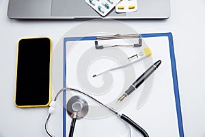 Medical desktop with stethoscope, pen, thermometer, smartphone and laptop close-up