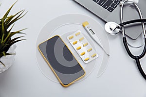 Medical desktop with stethoscope, pills, thermometer, smartphone and laptop