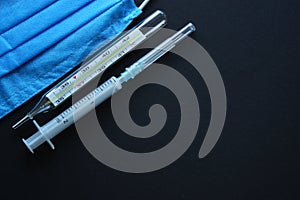 Medical devices. Protective surgery blue mask, syringe and thermometer on a black background. Copy space