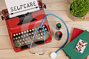 medical diagnosis - doctor workplace with blue stethoscope, pills, red typewriter with text Selfcare