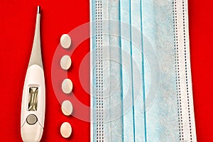 Medical digital thermometer on red background with pills and mask