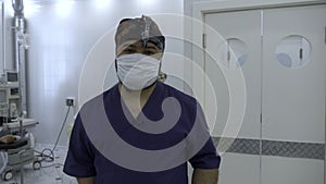 Medical doctor with a binocular magnifier in a mask. Action. Background of an operating theatre.