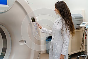 Medical doctor does computer tomography fot patient. Young girl in white coat presses button on CT.