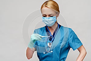 Medical doctor nurse woman with stethoscope wearing protective mask and rubber or latex gloves holding thermometer