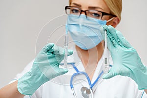 Medical doctor nurse woman wearing protective mask and gloves - holding electronic thermometer and syringe