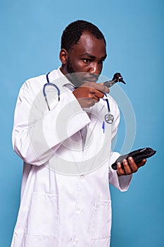 Medical doctor in white lab coat with stethoscope looking worried at otoscope
