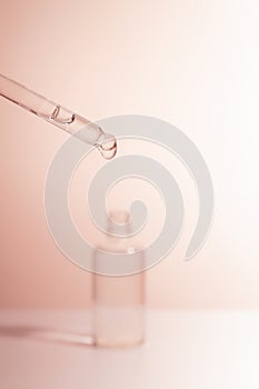 A medical dropper with liquid and a drop falling over a bottle of essence, serum or care oil in the bathroom against a
