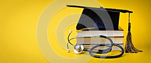 Medical education - college graduation cap with stethoscope and books on yellow background with copy space