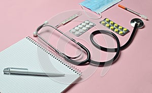 Medical equipment on a pink pastel background. Blisters pills, notepad, stethoscope, thermometer. Medical concept, top view, flat.