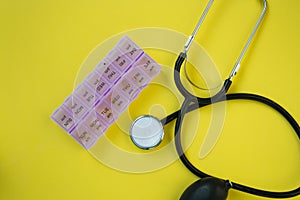 Medical stethoscope and blood pressure meter with container for pills for each day of the week, yellow background, healthcare
