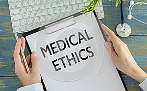 Medical Ethics text with document brown envelope and stethoscope isolated on office desk.