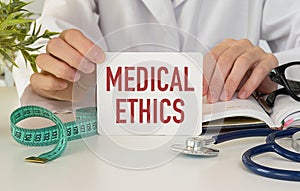 Medical Ethics text with document brown envelope and stethoscope isolated on office desk