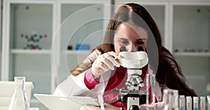 Medical examiner looks through a microscope and writes notes for information about experiment or research in laboratory