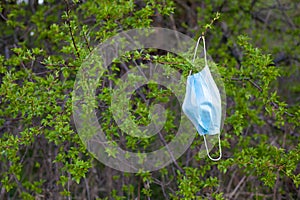 Medical face mask hanging on a tree. Ecology, environmental pollution due to the covid-19 pandemic