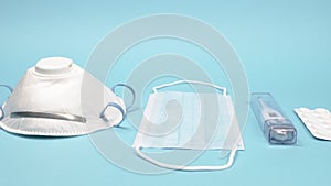 Medical face mask, respirator, thermometer and pills on a blue background.