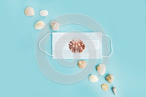 Medical face mask and seashells on blue background. Flat lay, copy space, holiday cancellation, pandemic, tourism