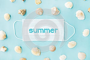 Medical face mask and seashells on blue background. Flat lying, copy space, holiday cancellation, pandemic, tourism