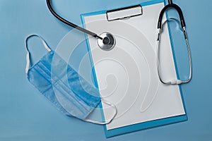 Medical face mask, stethoscope and blank document on blue background. Copy space. Mock up